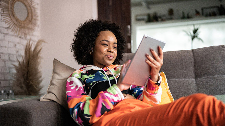 Moça negra sentada ao sofá navegando na internet com um tablet