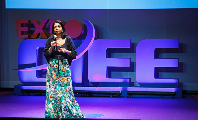 Fundo com o logo da Expo CIEE em 3D, a frente temos a imagem de uma mulher falando com um microfone na mão.